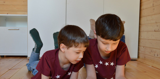 Zwei Jungen liegen auf dem Boden und gucken auf das Tablet, welches der rechte in seiner Hand hält.